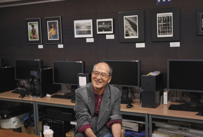 講師の方の作品とデジタル写真のための PC機材の前で語る尾辻さん。